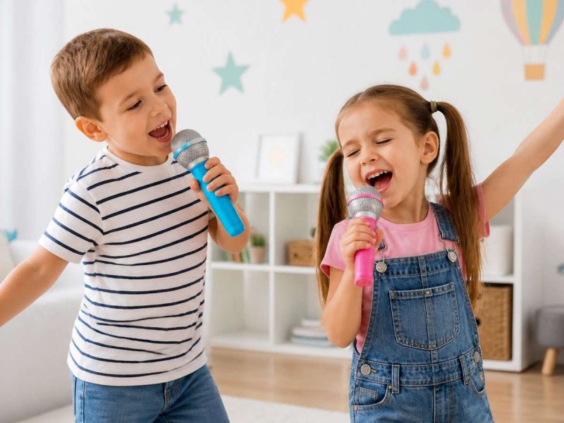 Two kids singing on toy microphones in a playroom